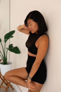 Woman in a seated yoga pose with a calm expression, leaning against a studio wall