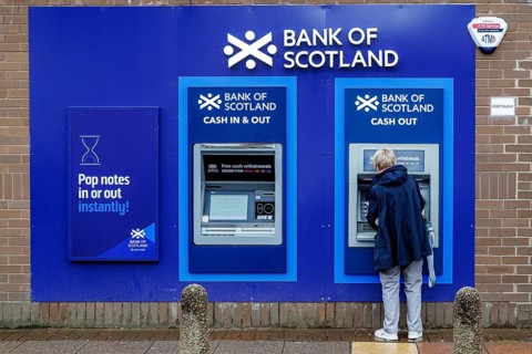 Woman using an outdoor Bank of Scotland ATM to withdraw cash on a street in Partick, Glasgow,
