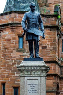 Close up detail of the blackened bronze statue of Sir William Pearce holding a design plan, Govan