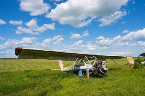 An old aircraft without an engine is resting on a vast green area under a cloudy sky, PZL-104 Wilga