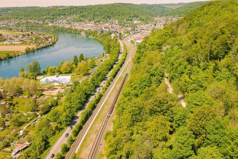 Wide aerial view of a landscape with river, railroad and wooded hills near a city, construction