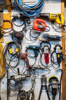 Various electric power tools including drills, circular sanders, jig saw hanging on white pegboard