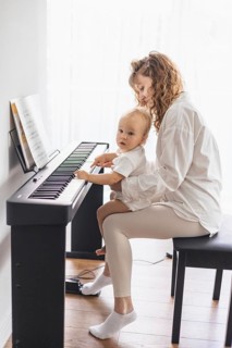 Mother and child sitting at a piano, engaging in a music activity together in a bright room