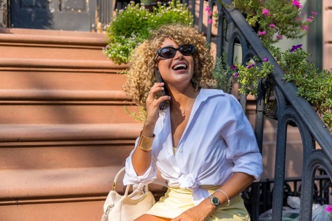 Young woman with curly blonde hair smiling and laughing while talking on her phone, sitting on