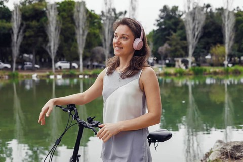 A young Caucasian woman with brown hair stands beside a bicycle near a serene lake. She wears pink