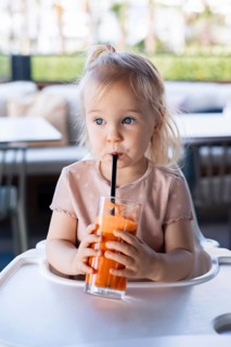 Girl toddler drinking carrot juice in cafe