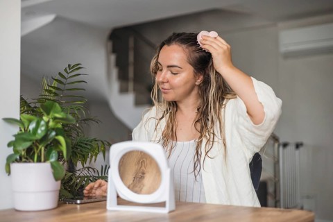 A woman is applying hair treatment while seated at a table with plants in a relaxed space