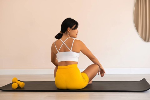 A woman sitting relaxed with dumbbells beside her on a yoga mat in a calm setting