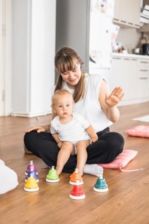 A woman and a baby seated on the floor, engaged playfully with colorful bells