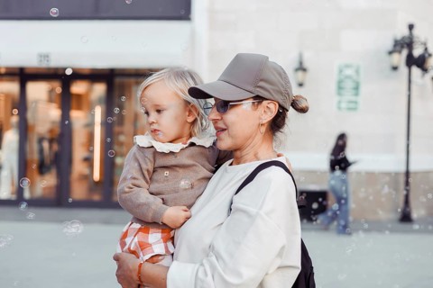 A woman holds her young daughter close as they watch bubbles float in the air. The city square is