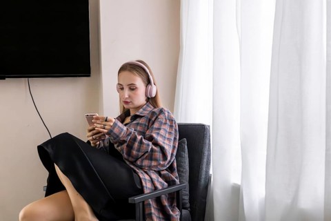 Young Caucasian woman with long brown hair, wearing headphones, sitting in a chair and using a