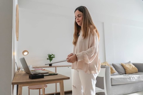 Woman standing and adjusting portable LED light panel for filming setup, home desk with laptop