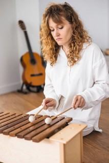 Woman playing marimba with a guitar in the background on a wooden floor