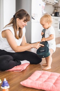 A mother guides her toddler during a playful music session with a ukulele