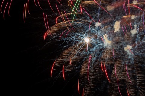 Red, orange and golden fireworks plus puffs of white smoke light up a black sky at night in summer,