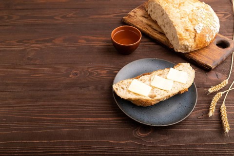 Slice of homemade bread with butter on plate on brown wooden background, cup of tea, copy space,