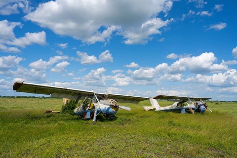 Two abandoned aircraft stand in a green field against a cloudy sky, PZL-104 Wilga multi-purpose