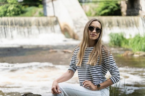 A woman in sunglasses, a striped top and white jeans near the river against the backdrop of the