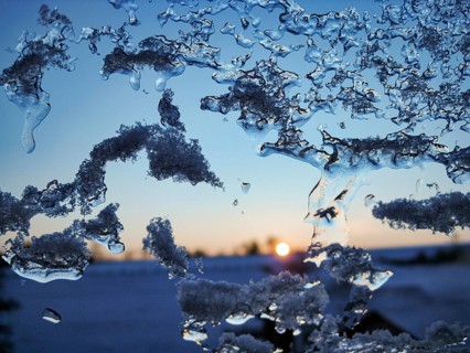 Close-up of ice crystals and frost structures on a glass panel, frozen skylight in winter, sunset