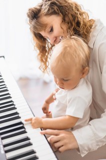 A woman gently teaches a baby at the piano, pointing at the keys with care