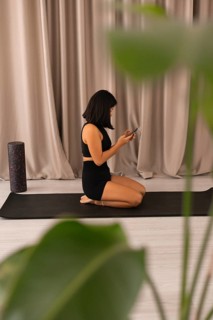Woman seated on yoga mat, using a phone, integrating technology with a serene indoor setting