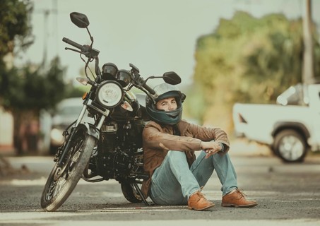 Portrait of a young motorcyclist leaning against his motorcycle on the road. Portrait of a handsome