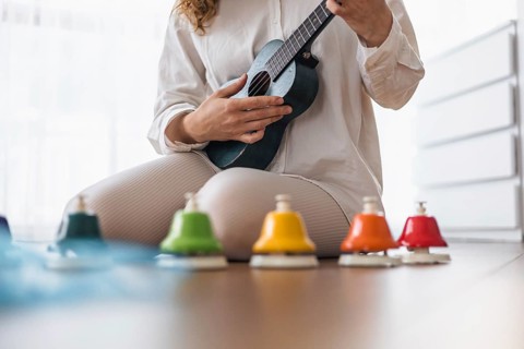 A woman in white playing a ukulele surrounded by colorful bells