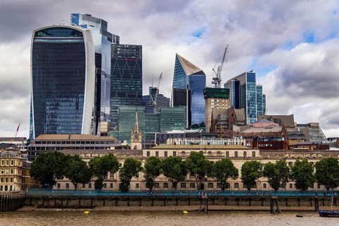 The neoclassical facade of Custom House fronts the Thames beneath a modern City of London skyline,