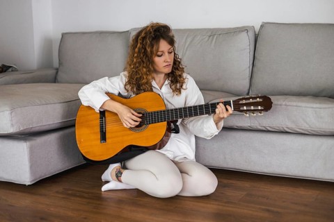 Woman sitting on the floor in a relaxed posture, playing an acoustic guitar at home