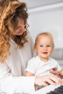 Mother and child interact warmly with piano keys, showcasing mutual affection