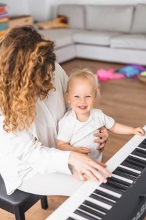 Child smiling while sitting on mother's lap as she plays the piano, depicting joy and interaction