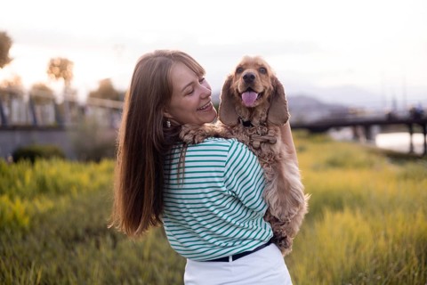 A happy woman embraces her dog Cocker Spaniel while standing in a sunset-lit field