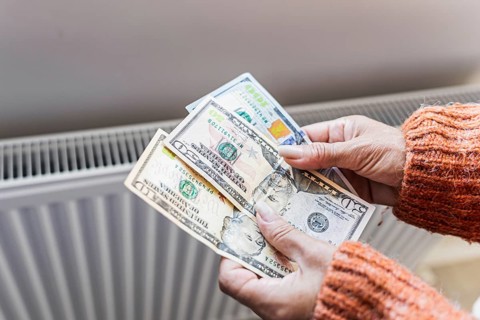 Woman holding US dollar banknotes near home radiator during winter heating season. Concept of