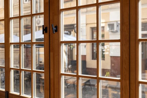 The warm ambiance of a cafe is highlighted by large wooden windows that frame a view of a lively