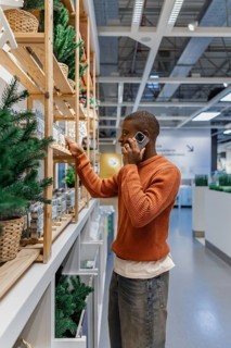 A man is standing in a store looking at home decor items on shelves. He is holding a phone to his