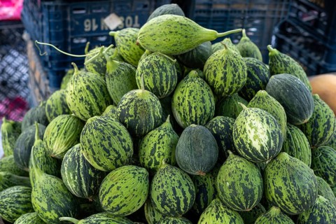 Cluster of striped green gourds stacked in black baskets at market