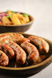 Close-up view of grilled sausages on wooden plate.Bowl with golden fries and onion in background