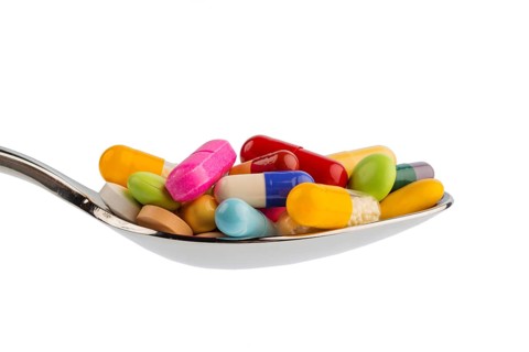 Lots of colorful tablets on a spoon. Symbolic photo for tablet addiction and misuse of medicines,