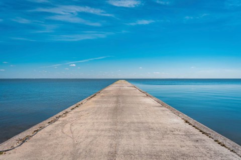 A long stone pier goes far into the sea against the background of a blue clear sky, A concrete pier