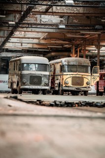 Two retro Mercedes trucks are parked in an abandoned hall surrounded by rust and industrial