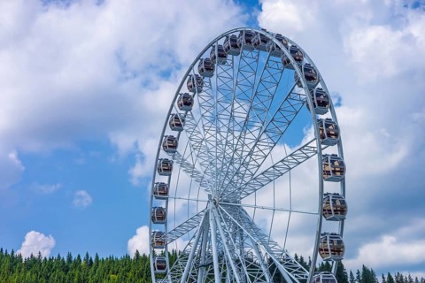 A large Ferris wheel stands against a blue sky with fluffy clouds. The structure is metallic and
