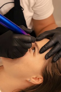 Close-up of microblading an eyebrow with a tattoo machine and gloves