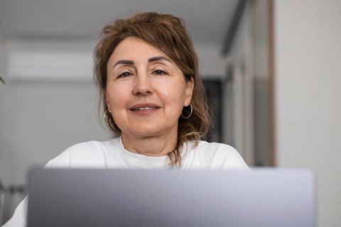 Portrait of mature woman sitting at home in the kitchen and using a laptop. Mid aged businesswoman
