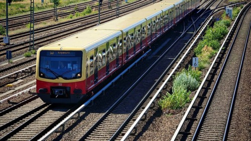 Red train on railroad tracks surrounded by vegetation in an urban environment, Berlin