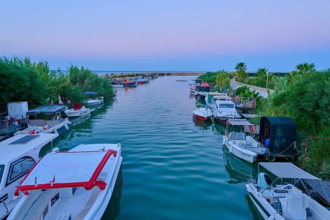 Boats are moored along a quiet river surrounded by lush vegetation at dawn, marina, Evrenseki,