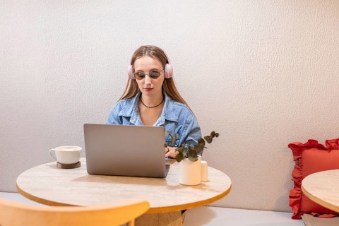 Young Caucasian woman with long brown hair wearing pink headphones, sitting at a table with a