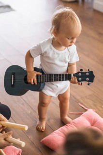 Child holding a guitar, focused on playing, on a wooden floor