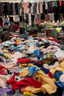 Piles of colorful clothes at a busy outdoor market stall