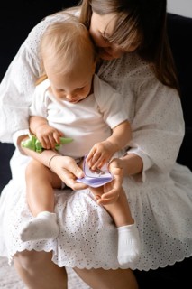 Woman in a white dress holding a baby with a toy, showcasing a nurturing bond