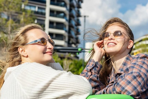 Two young Caucasian women with sunglasses enjoy a sunny day outdoors. One has long blond hair, and